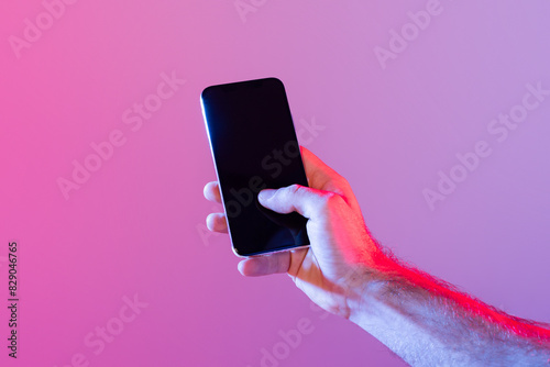 A person holds a smartphone with a dark, unlit screen against a gradient purple background. The lighting casts a soft, ambient glow, creating a modern and tech-savvy atmosphere.