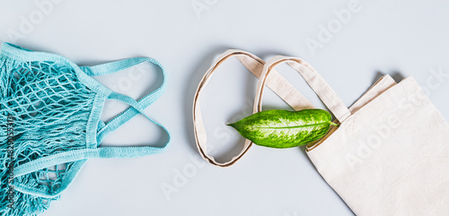 Eco friendly textile bag with fresh leaf and string bag on blue background top view web banner