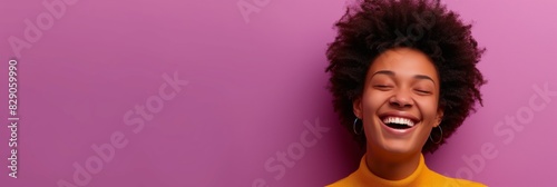 A young woman in a yellow turtleneck laughing heartily against a vibrant purple backdrop