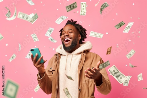 Overjoyed man celebrating financial success with falling dollar bills and smartphone on pink background