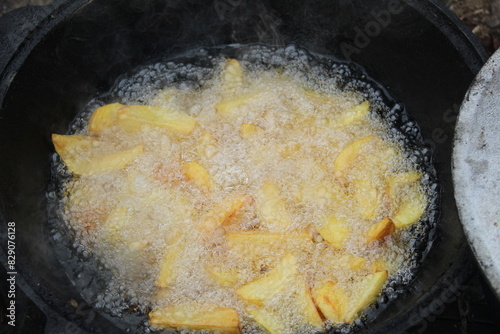 Potatoes are fried in a large pan in a cauldron, close-up view from above. Cooking in nature