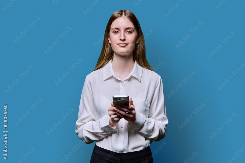 Teenage student girl in shirt holding smartphone in hands on blue studio background Teenage student girl in shirt holding smartphone in hands on blue studio background