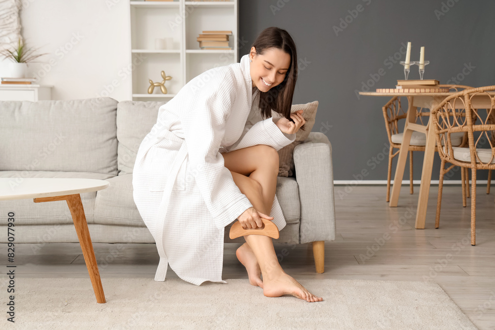 Young woman massaging her leg with wooden scraper on sofa at home Young woman massaging her leg with wooden scraper on sofa at home