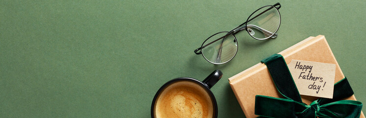 Happy Fathers Day banner template. Flat lay composition with gift box, glasses, coffee cup on green background. Top view with copy space.