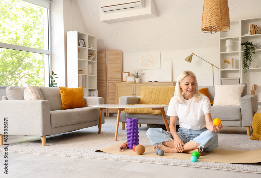 Mature woman with massage balls sitting on mat at home Mature woman with massage balls sitting on mat at home