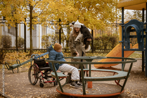a 10-year-old boy in a wheelchair walks in the fall with his mother on the street with a dog on the playground. High quality photo