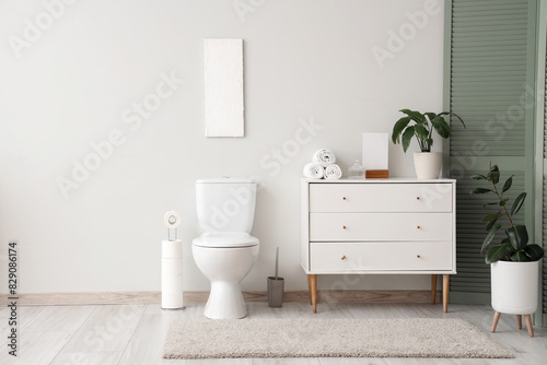 Interior of restroom with toilet bowl and chest of drawers near white wall