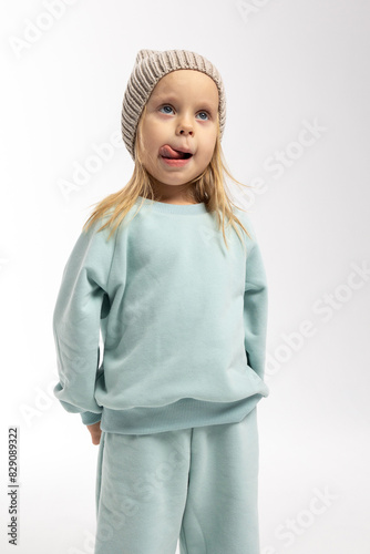 Portrait of beautiful cute little toddler girl. Child with funny face in mint sweatshirt and hat. Pretty smile kid in studio on white background.