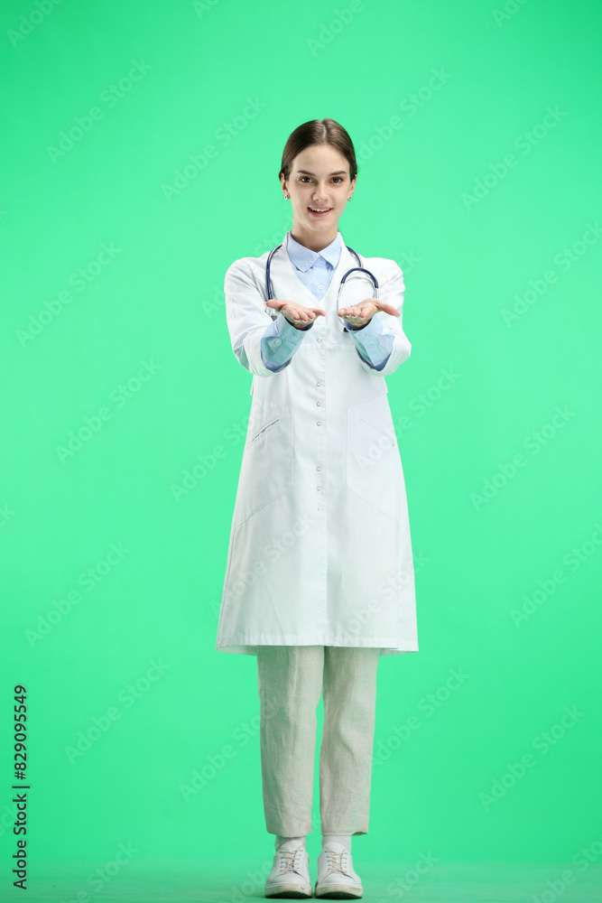A full-length female doctor, on a green background, points forward