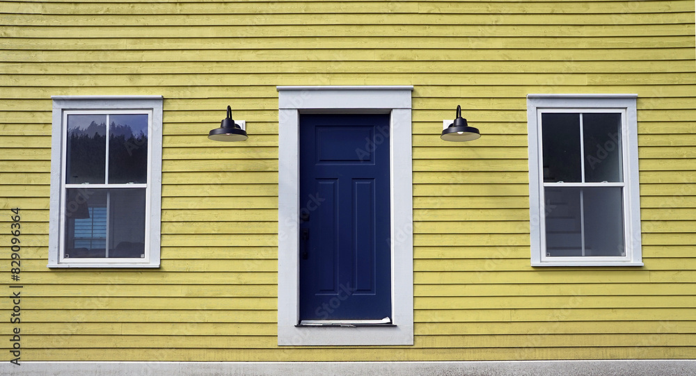 Facade of yellow clapboard house with door and two windows