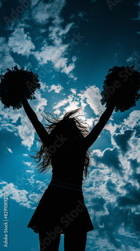 silhouette of a cheerleader with pom-poms against a bright cloudy sky