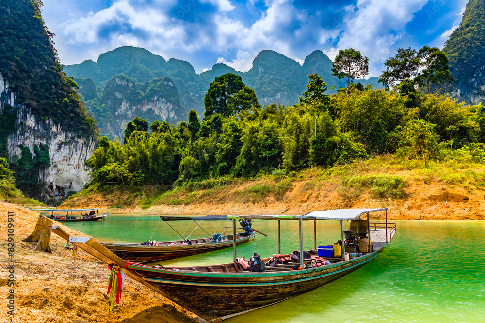 Naklejka premium Wooden longtail boats on the shore of a lake surrounded by rainforest and cliffs (Khao Sok National Park)
