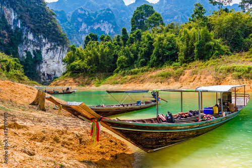 Longtail boats on the shore of a rainforest lake with towering limestone cliffs behind