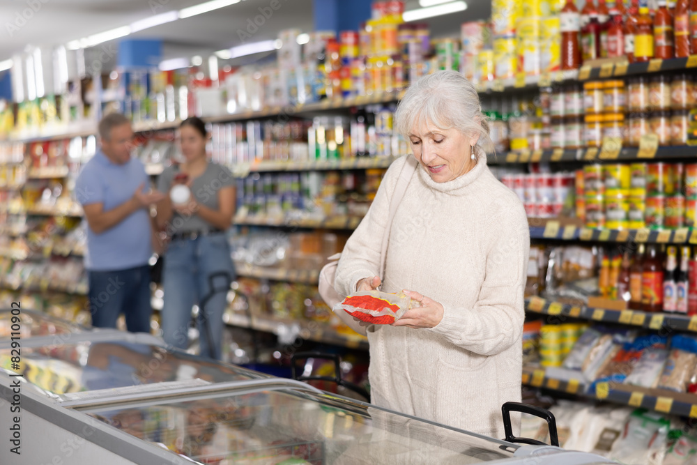 Elderly woman choosing frozen food in supermarket. Young woman purchasing goods in grocery store