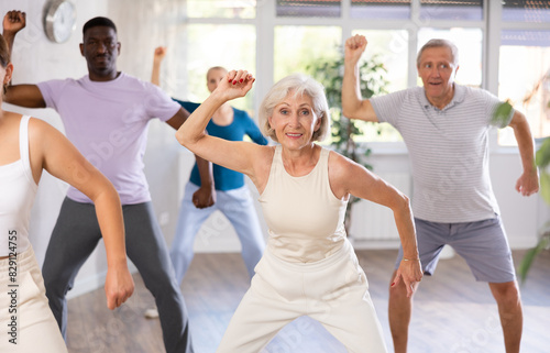 Elderly woman and small group of amateur dancers of different ages are actively engaged in fitness room. Physical activity, good bodily shape