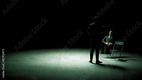 Man in suit in front of mirror. Stock footage. Man on stage with mirror puts on suit. Stage production with one man and mirror on dark stage