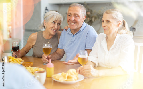 Group of happy seniors celebrating holiday drinking and chatting at table at home