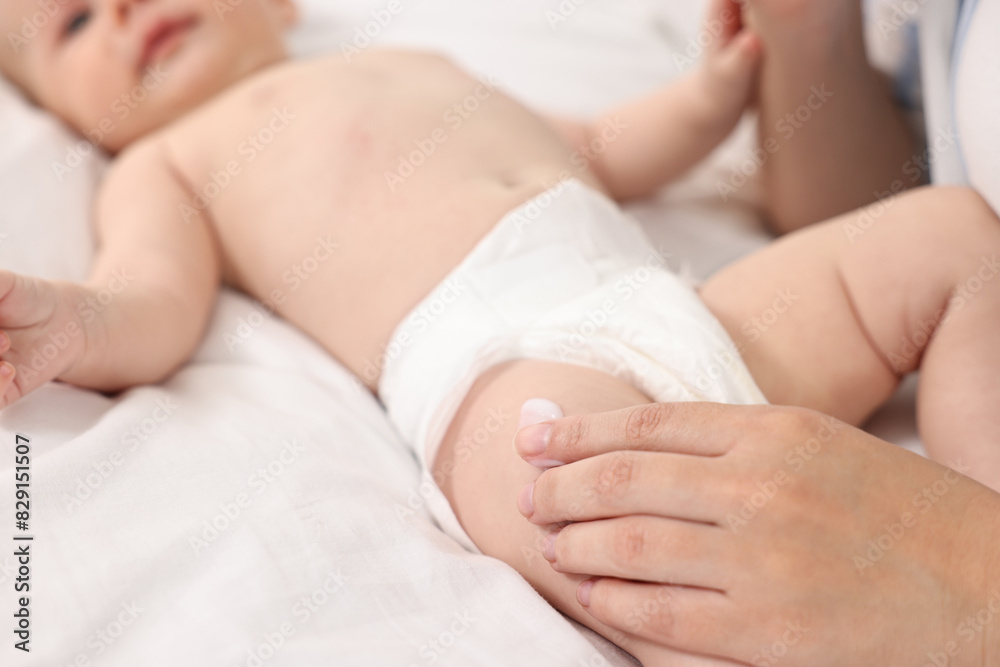 Woman applying body cream onto baby`s skin on bed, closeup Woman applying body cream onto baby`s skin on bed, closeup