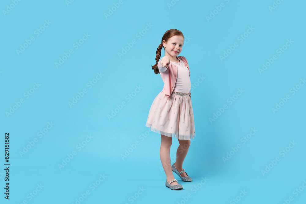 Cute little girl dancing on light blue background, space for text