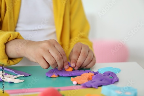 Little girl sculpting with play dough at table indoors, closeup