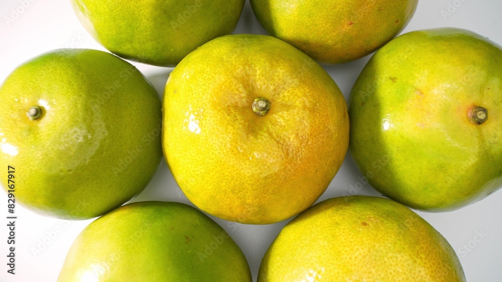 Fresh green oranges, tightly packed, their smooth surfaces reflecting light. The greenish-yellow tint suggests ripening, a visual feast of freshness. Orange fruit background.
