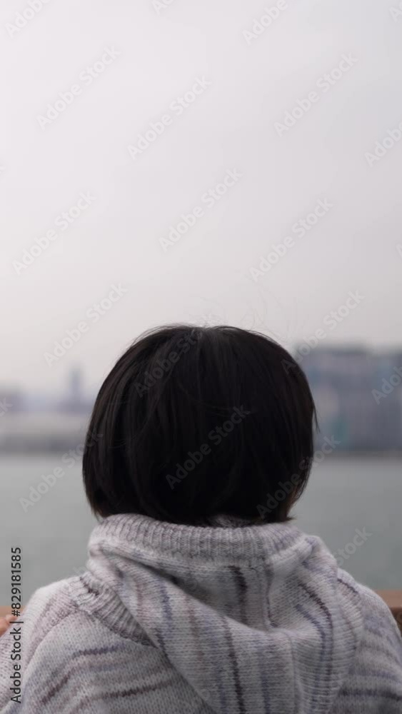 Captured in slow motion, a young woman leans on a railing by the water ...