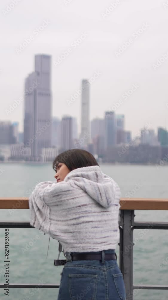 Captured in slow motion, a young woman leans on a railing by the water ...