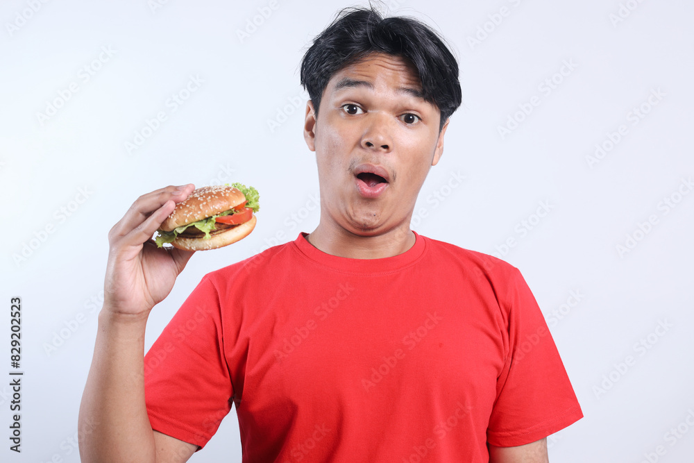 Potrait Of Suprised Young Asian Man Raised Hand While Holding Burger Isolated On White Background Potrait Of Suprised Young Asian Man Raised Hand While Holding Burger Isolated On White Background