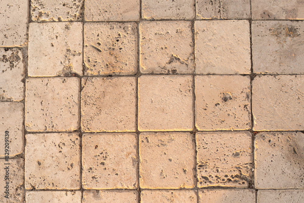 Obraz premium The detail of worn stone paving blocks, showcasing their texture and the subtle color variations due to weathering. The natural light enhances the stones sandy tones