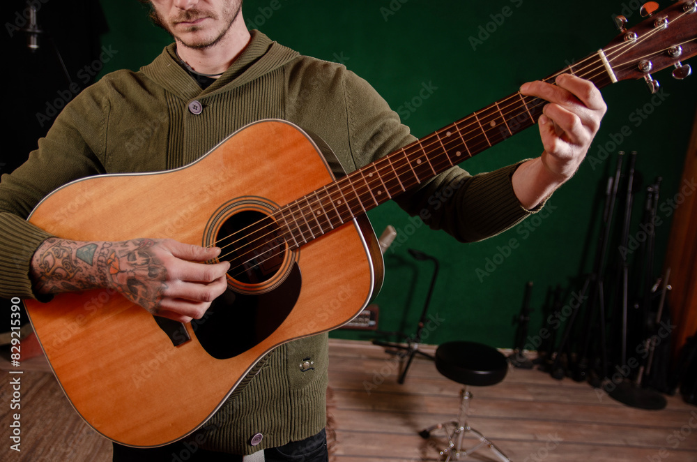 Obraz premium Bearded charismatic guy playing acoustic guitar in the music studio