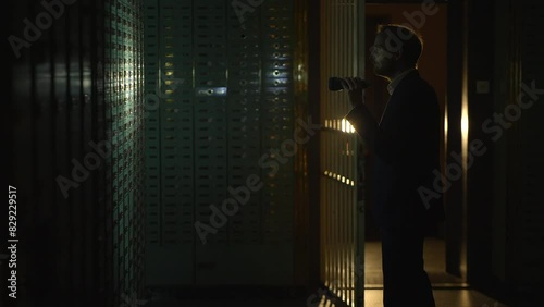 Man in suit spies Investigating vault safe holding a flashlight in dark room