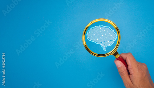Hand holding a magnifying glass with a brain icon against a blue background.