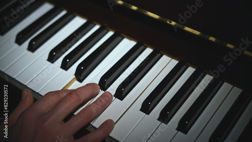 Close-up of hand playing piano. Media. Light falling on hand playing piano. Lonely hand is playing notes on piano