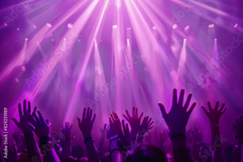Fans hands raised at concert with purple light rays in the background