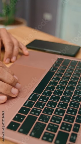 In a professional office setting, hands are seen typing on a laptop with a smartphone on the desk