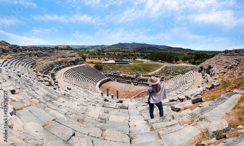 Happy woman in hat open arms in free happiness standing and posing - Ancient roman theater at Miletus in southern Turkey photo