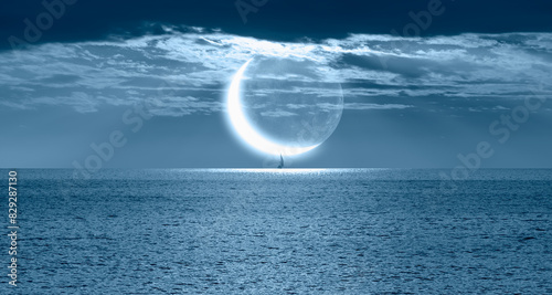 A lonely yacht sails on the sea,  Crescent or new moon  in the background  photo