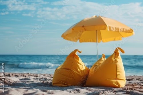 Two yellow bean bags and a beach umbrella on the sand representing summer vacation