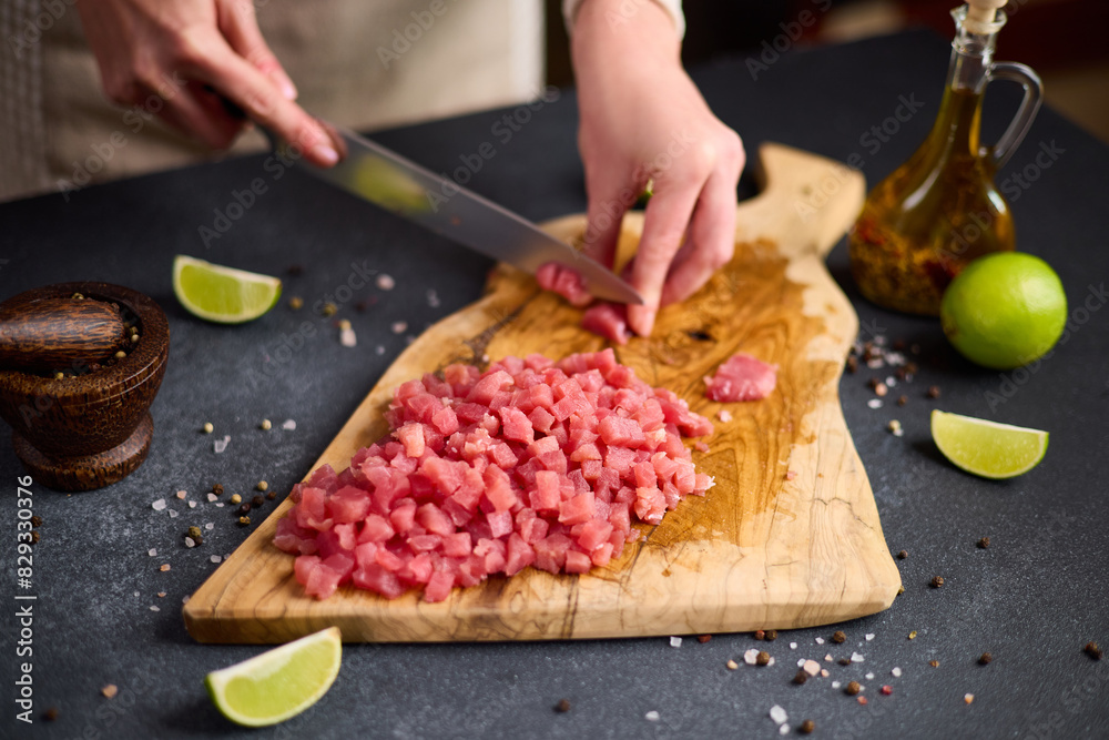 Woman cut tuna steak into slices on a wooden cutting board at domestic kitchen