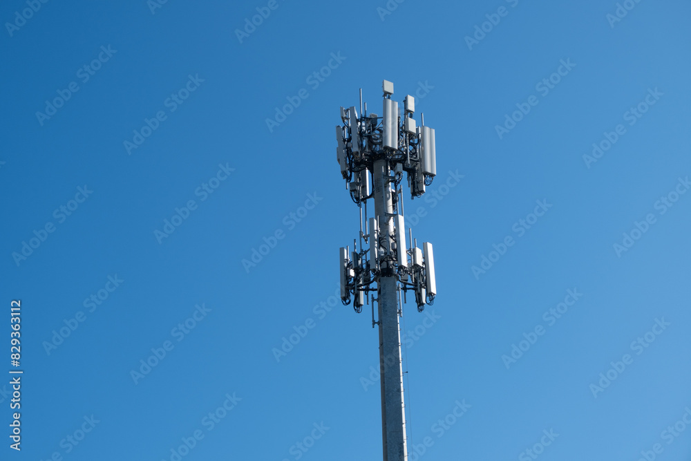 A cell tower or cell site, cellular base station, mounted with electric communications equipment and antennae for wireless communication, against blue sky.