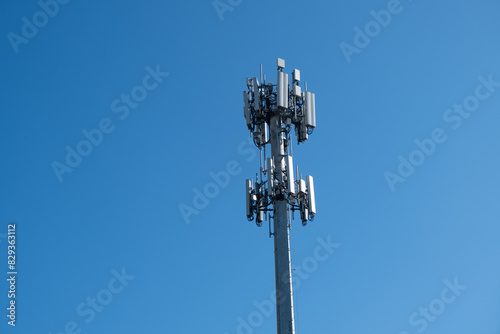 A cell tower or cell site, cellular base station, mounted with electric communications equipment and antennae for wireless communication, against blue sky.