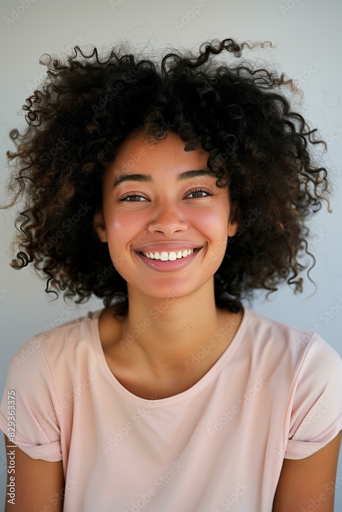 woman with curly hair smiling, wearing a light pink shirt, light grey background. woman with curly hair smiling, wearing a light pink shirt, light grey background.