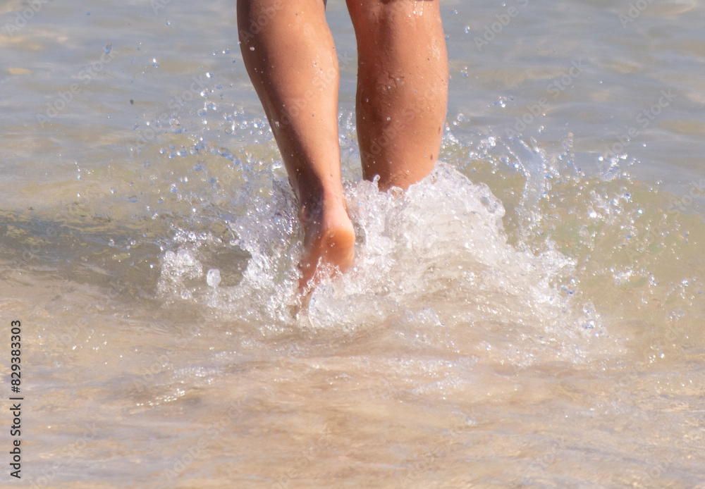 Legs of a girl walking on the water on the sandy beach of the sea