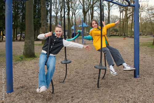 Two teenage girls 10-12 years old on a hanging swing have fun riding in a spring park for walks