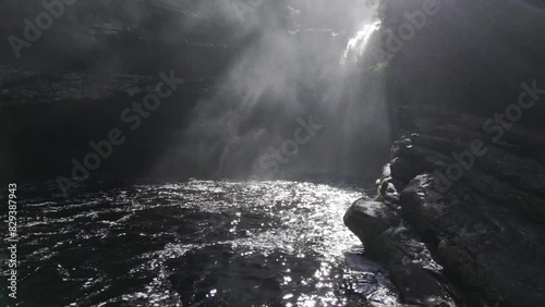 Drone flies from pool at bottom to middle of Sossego waterfall into the sunlight behind the waterfall photo