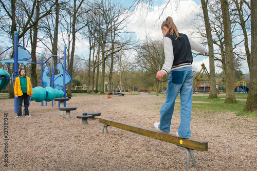 Two teenage girls on the crossbar for walking in the park with a simple swing for children