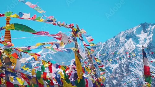 Slow motion shot of Buddhist prayer flags waving in the wind in front of the snow covered Himalayan mountain peaks as seen from Kunzum La on the way to Spiti Valley in Himachal Pradesh, India. photo