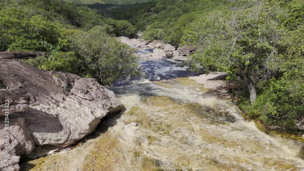Drone hovers over top part of natural water slide facing the pool below