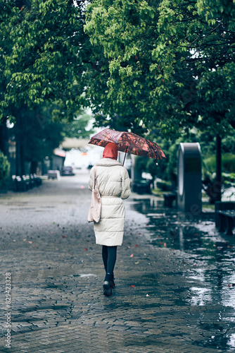 A young woman walks with her back to the camera with an umbrella. A walk through the rainy city. With space to copy. High quality photo