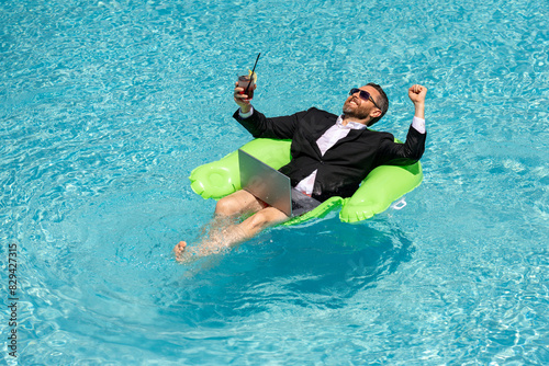 Successful business man in suit in pool water. Business man in suit working on laptop in swimming pool. Travel tourism and business concept. Crazy male office business employee using laptop.